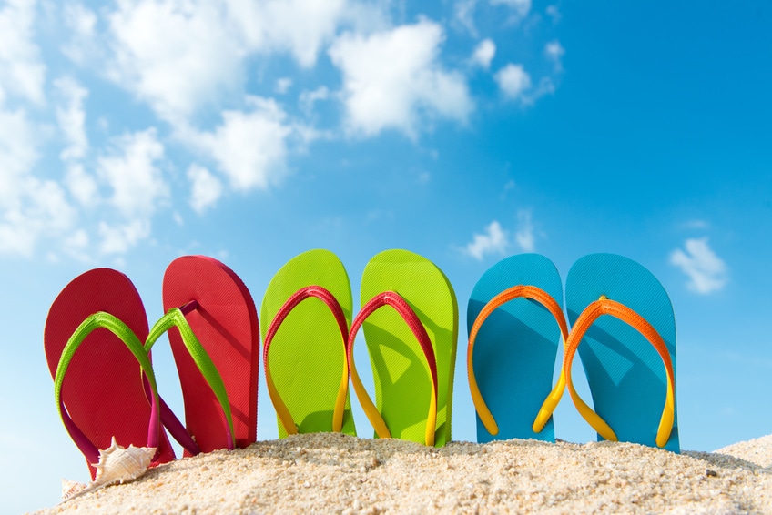 Row of colorful flip flops on beach against sunny sky