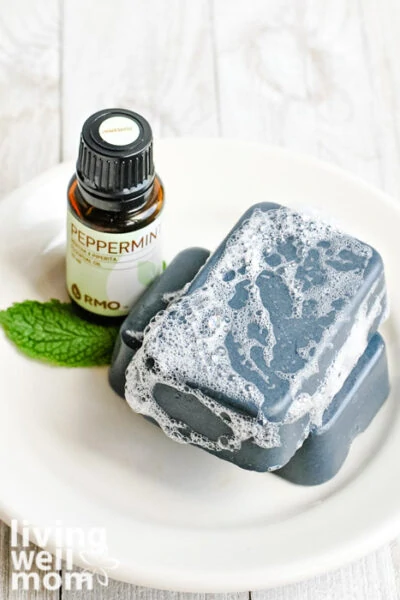 Bar of charcoal soap on a plate next to a bottle of peppermint essential oils