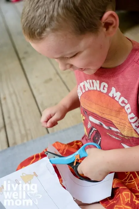 A 4 year old boy holding a pair of blue safety scissors, cutting along a straight line on paper.