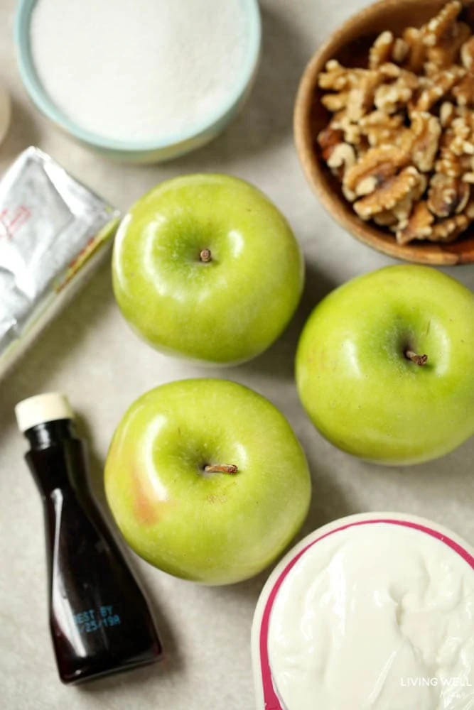 Green apples on a baking sheet, with vanilla extract, sugar, nuts and sour cream nearby.