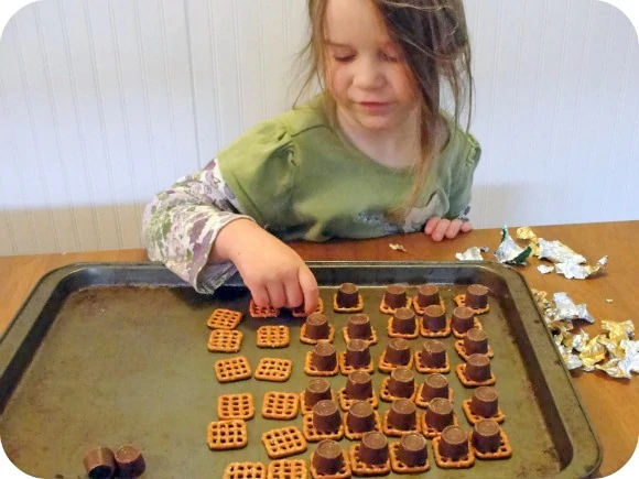 little girl putting chocolate onto pretzel squares 