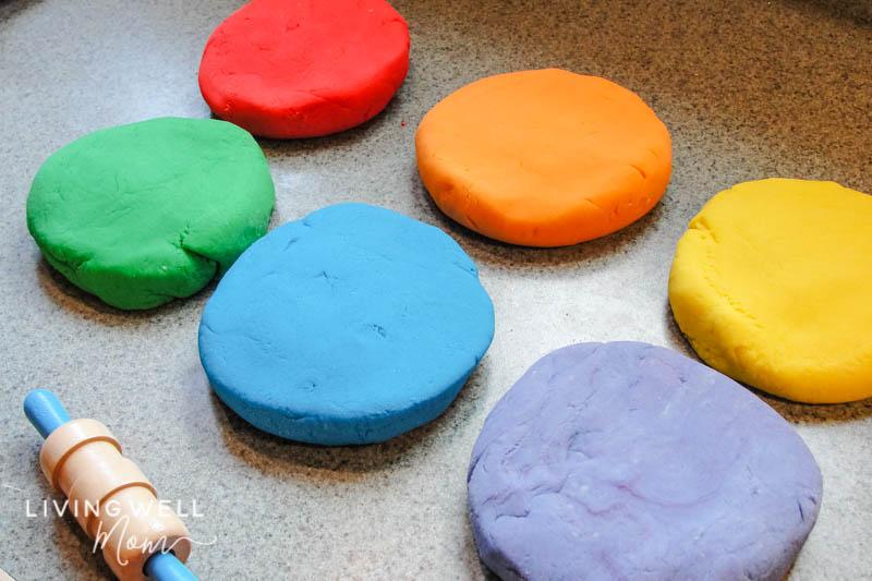 Flattened balls of DIY playdough on a countertop, with a rolling pin nearby. 
