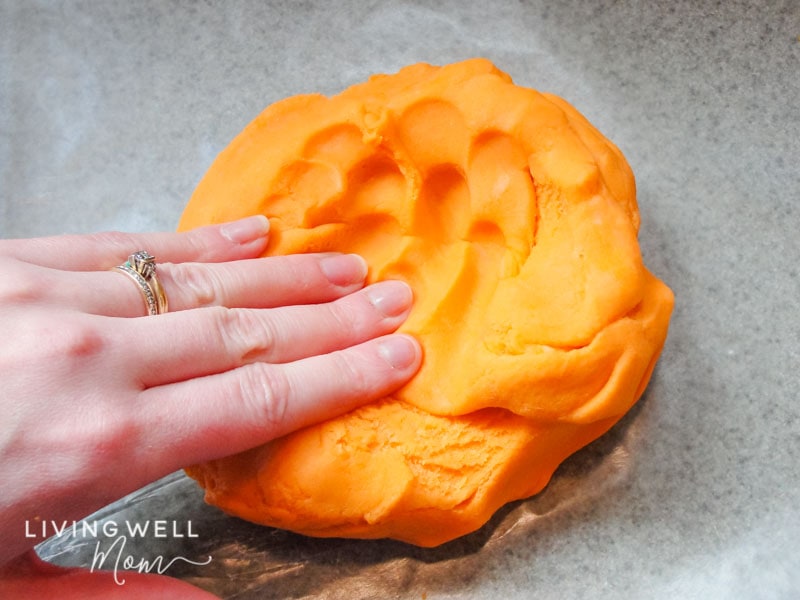 A hand pressing into soft, orange playdough.