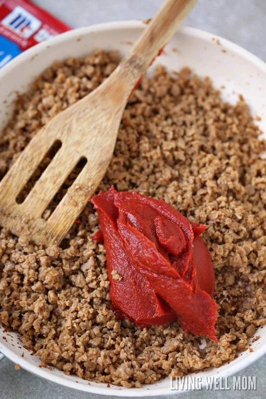 A skillet of cooked ground beef, with tomato paste being mixed in 