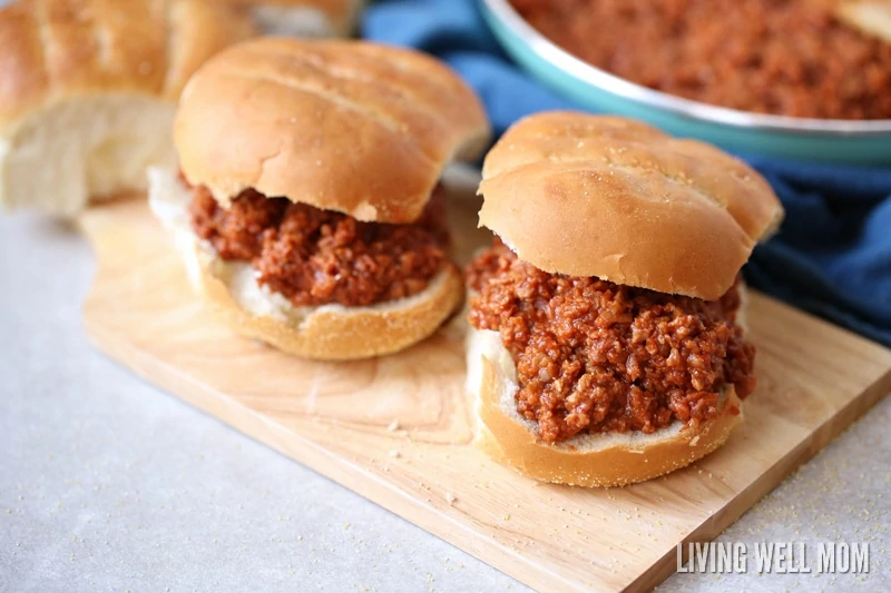 Two sloppy joe sandwiches on a wooden cutting board. 