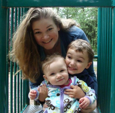 a woman holding a toddler and a baby on a playground 