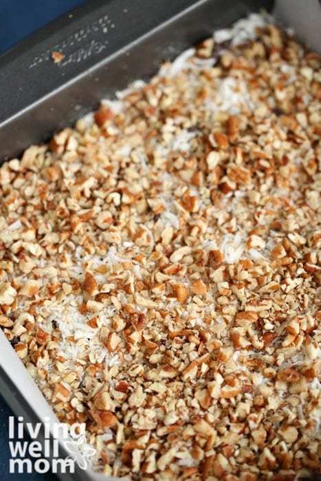 nuts on top of coconut flakes and chocolate chips and butterscotch chips in a pan 