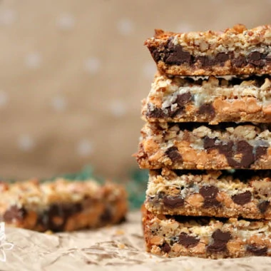 stack of magic cookie bars with beige spotted background and coconut flakes