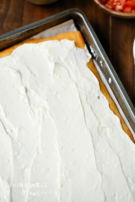 spreading a sour cream and cream cheese mixture over baked dough