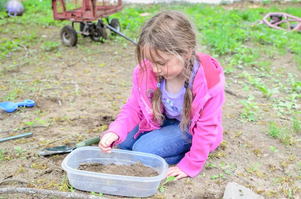 A girl filling a plastic container with dirt. 