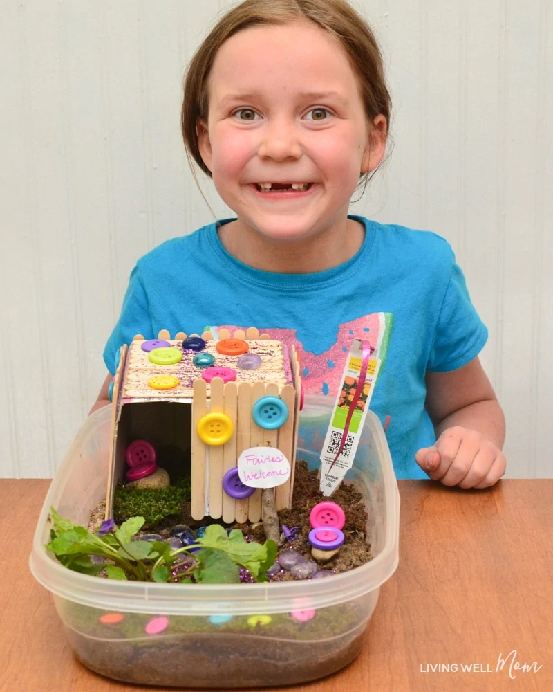 A little girl sitting at a table with a homemade fairy house craft project. 
