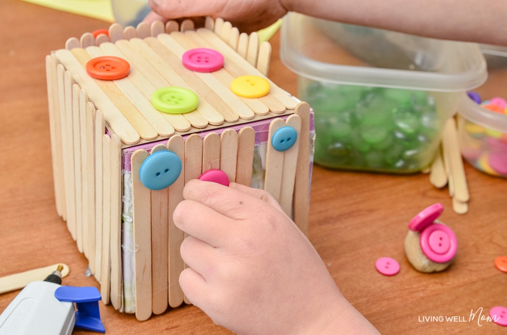 Buttons being glued onto a homemade fairy home. 