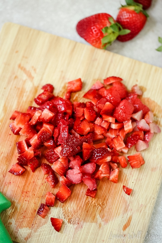 Fresh strawberries chopped into small chunks on a wooden cutting board. 