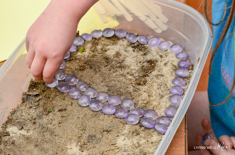 Lining a dirt filled bin with purple stones. 