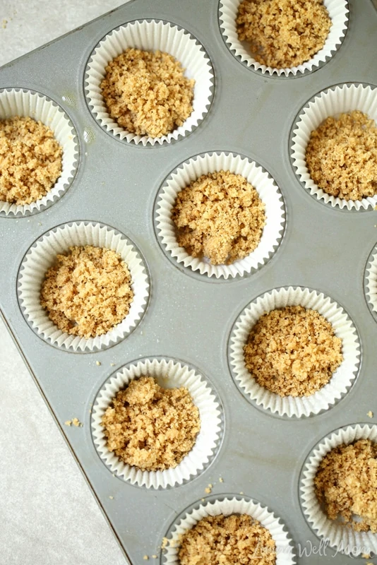 Graham cracker crumble in liners placed inside of a muffin tin. 