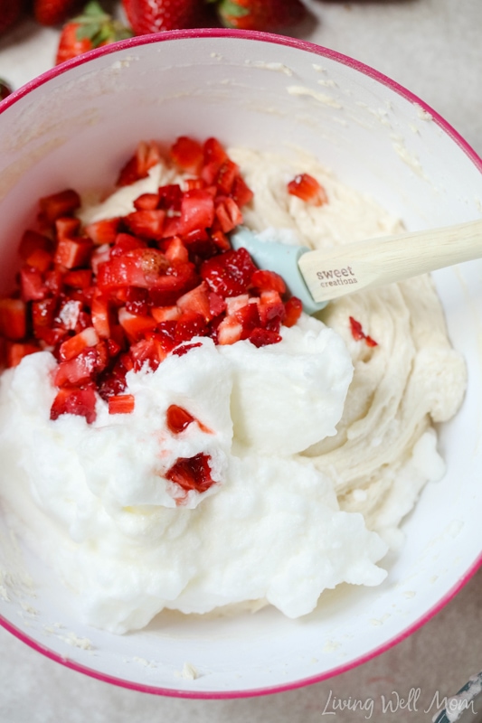 Freshly chopped strawberries and egg whites being stirred into cupcake batter. 