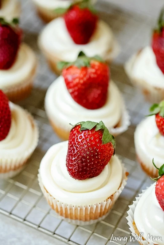 Whole strawberries atop a strawberry cheesecake cupcake. 