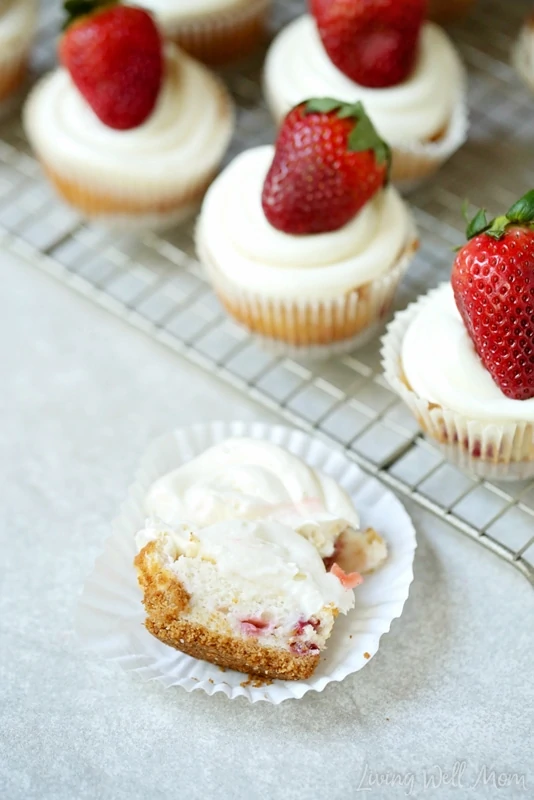 A cupcake cut in half, showing the graham cracker crust and strawberries inside the freshly baked cake. 