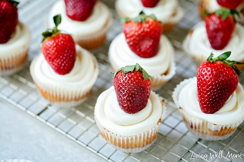 Finished cupcakes on a cooling rack with strawberry filling and cheesecake icing. 