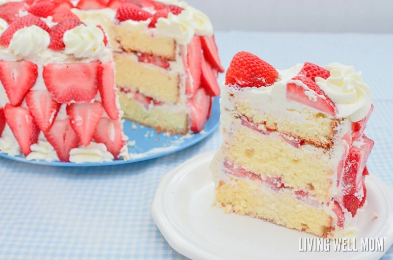 slice of strawberries and cream cake with the rest of the cake in the background