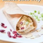 cranberry chicken salad in a wrap on white plate with celery, almonds, and dried cranberries