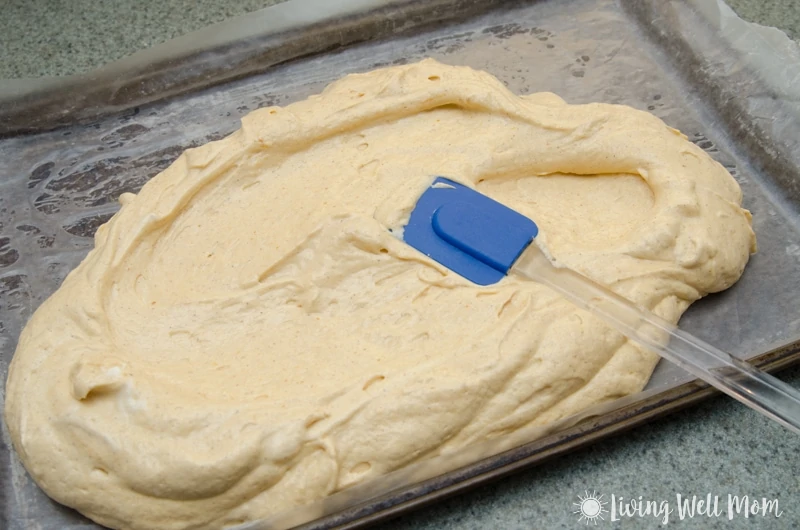Rubber spatula spreading cake batter onto a baking sheet lined with parchment paper