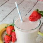 strawberry smoothie with straw and banana in a glass on white wood background