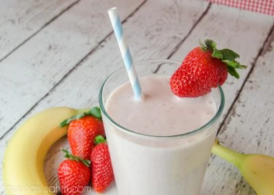 strawberry smoothie with straw and banana in a glass on white wood background