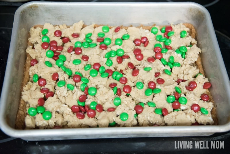 Adding M&Ms to the top layer of the candy cookie bars.