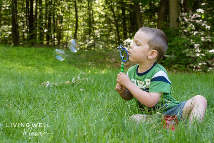 A boy blowing homemade bubble solution through a wand; 2 bubbles float in the air. 