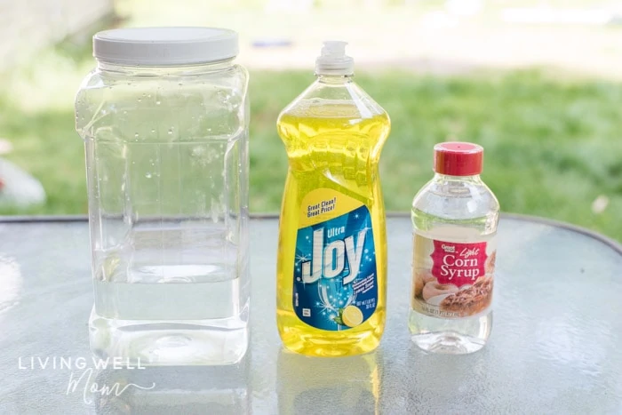 Ingredients lined up on a table for making homemade DIY bubble recipe; water, dish soap and corn syrup.