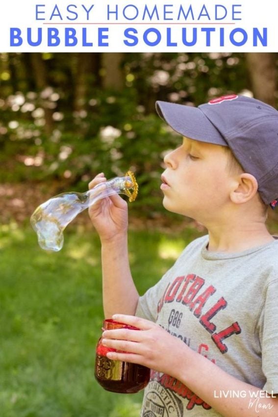 A kid blowing a bubble through a pipe cleaner wand, with a jar of DIY bubble solution in his other hand. 