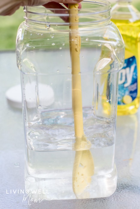 A wooden spoon stirring homemade bubble recipe ingredients together in a large container. 