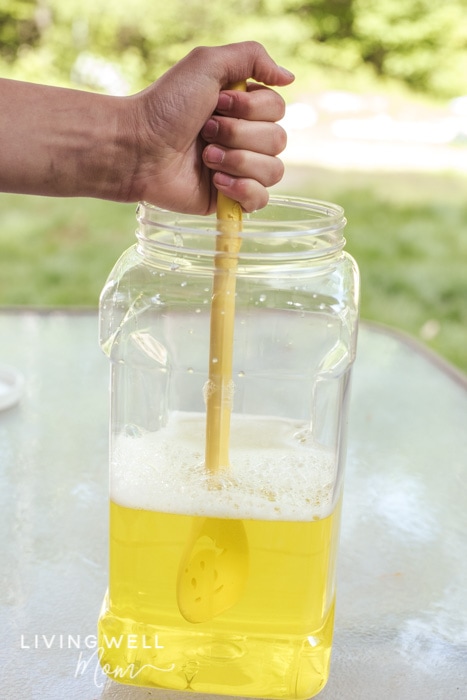 Mixing homemade bubble solution with a wooden spoon in a large plastic container. 