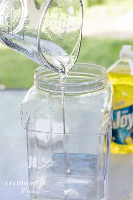 Measuring cup of corn syrup being poured into a large plastic container of water. 