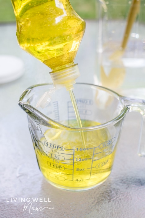 Yellow dish soap being dispensed into a glass measuring cup.