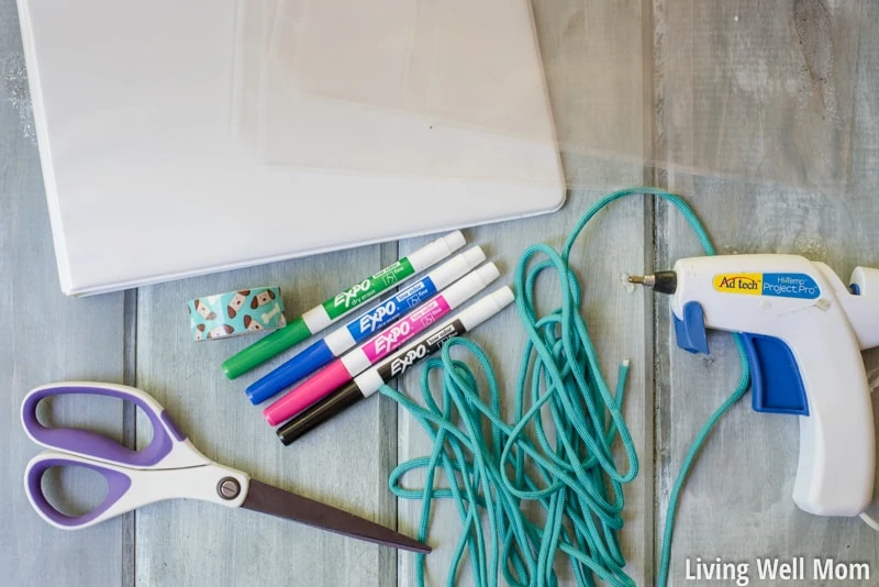 Supplies for creating DIY kids travel binder including binder, scissors, tape, glue gun, string and dry erase markers. 