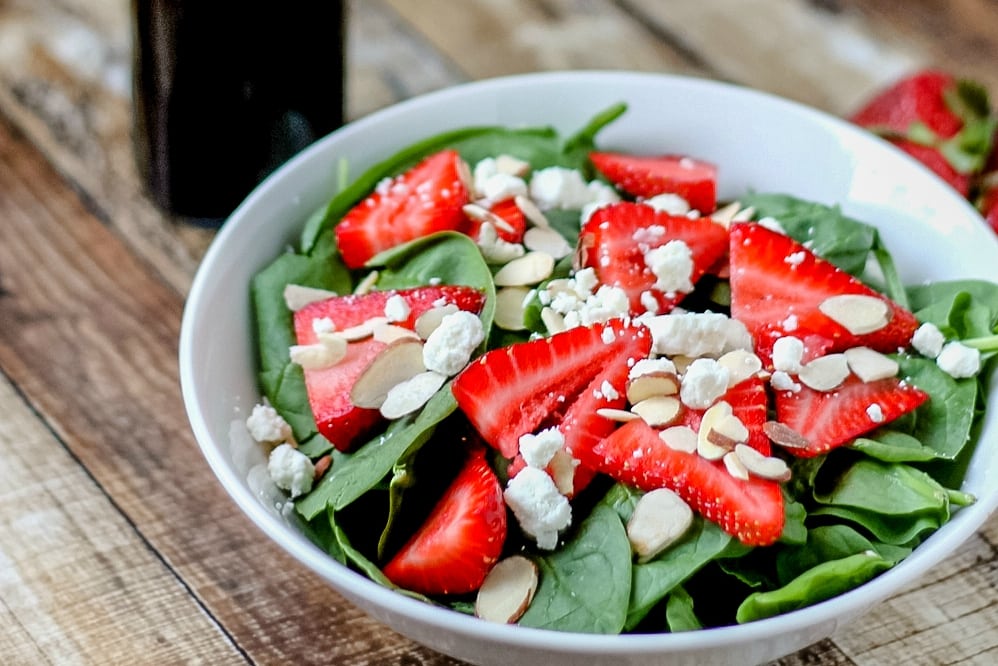 spinach salad topped with goat cheese and sliced strawberries