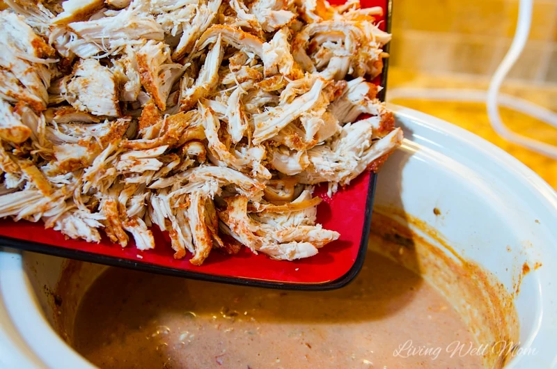 Shredded chicken being added to a slow cooker