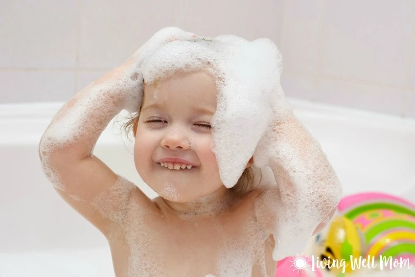 child with shampoo sudsy hair smiling in bathtub