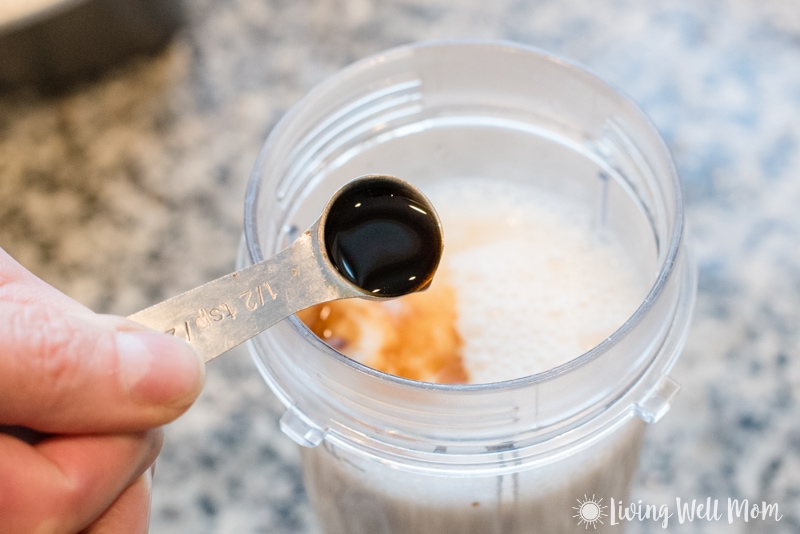 teaspoon with vanilla extract pouring into milk in plastic blender cup