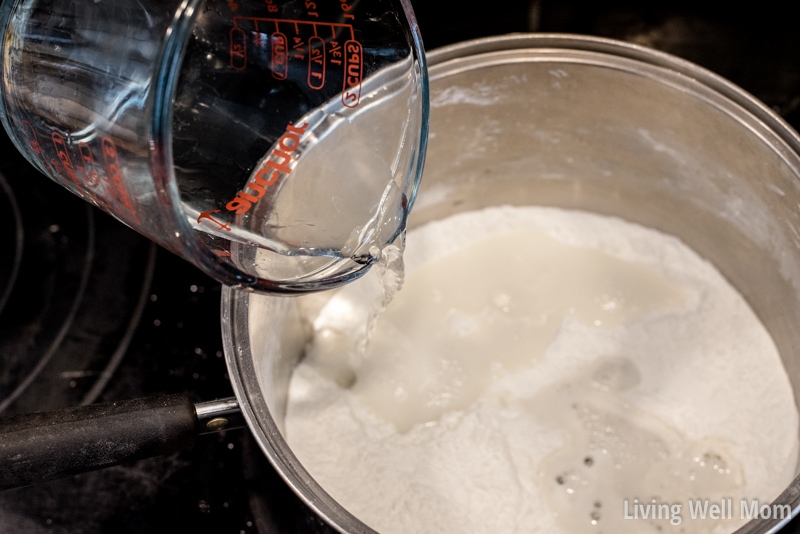 Adding a measuring cup of water to homemade play dough mixture