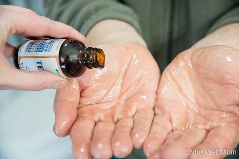 adding tea tree oil to hands covered in coconut oil for natural dandruff remedies