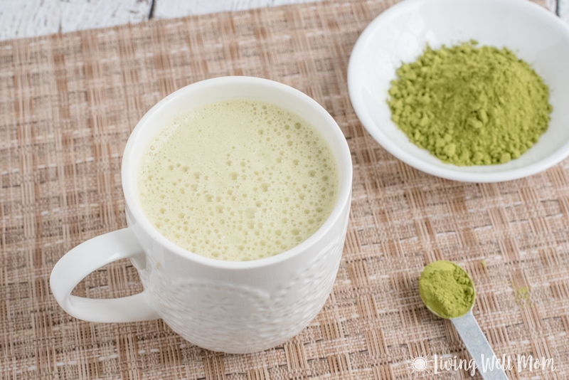 white mug with matcha green tea latte, white bowl with matcha powder and spoon