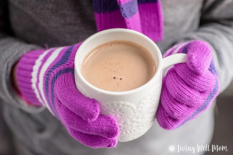 Child in gloves and scarf holding a cup of hot chocolate