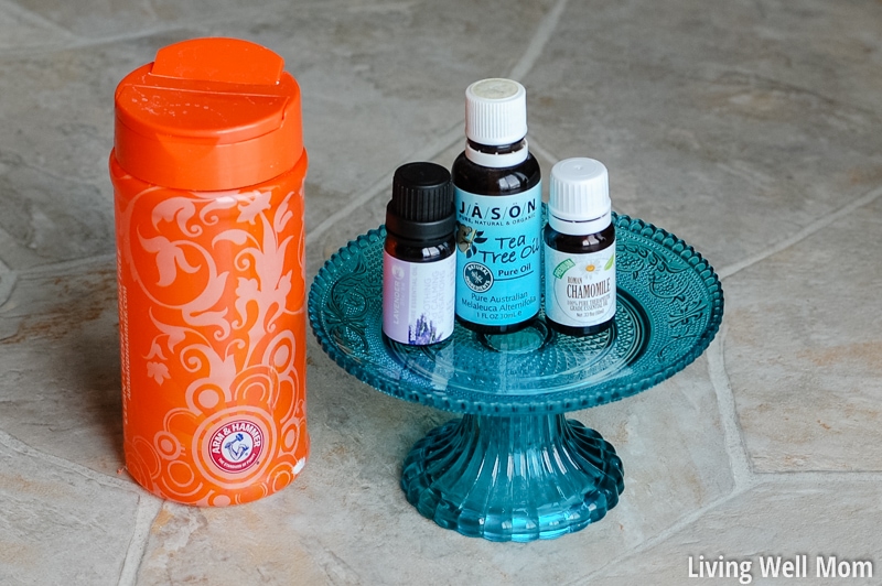 A cake stand with essential oil bottles on top and a container of baking soda nearby, for making DIY carpet deodorizer.