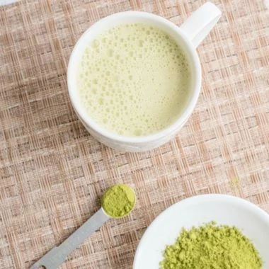 white mug with matcha latte and matcha green tea powder in white bowl and spoon