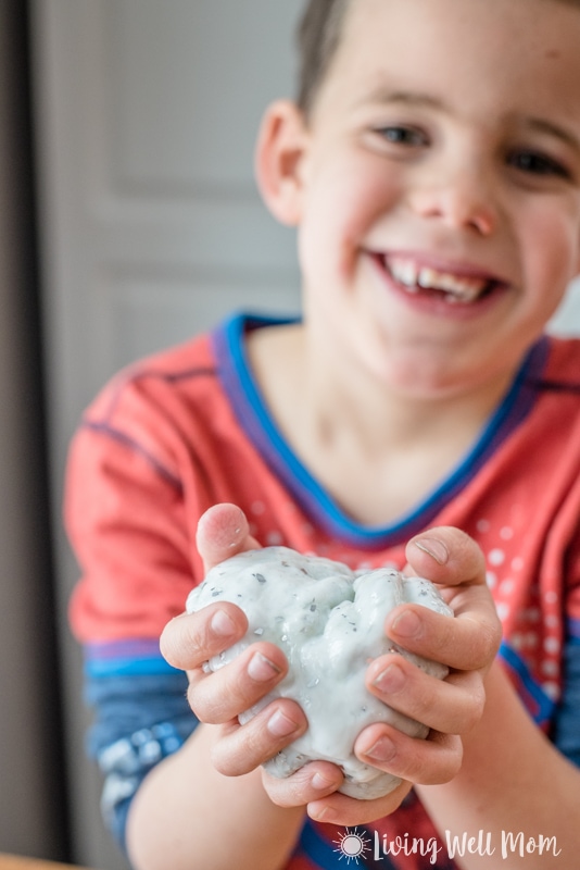 a boy smiles in the background while holding a ball of DIY slime 