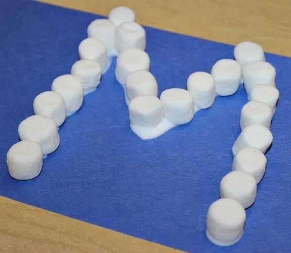 marshmallows glued to a blue construction paper In the shape of an M 