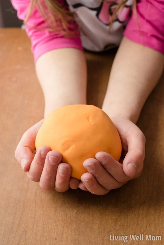 A girl cupping a large ball of orange dough in her hands